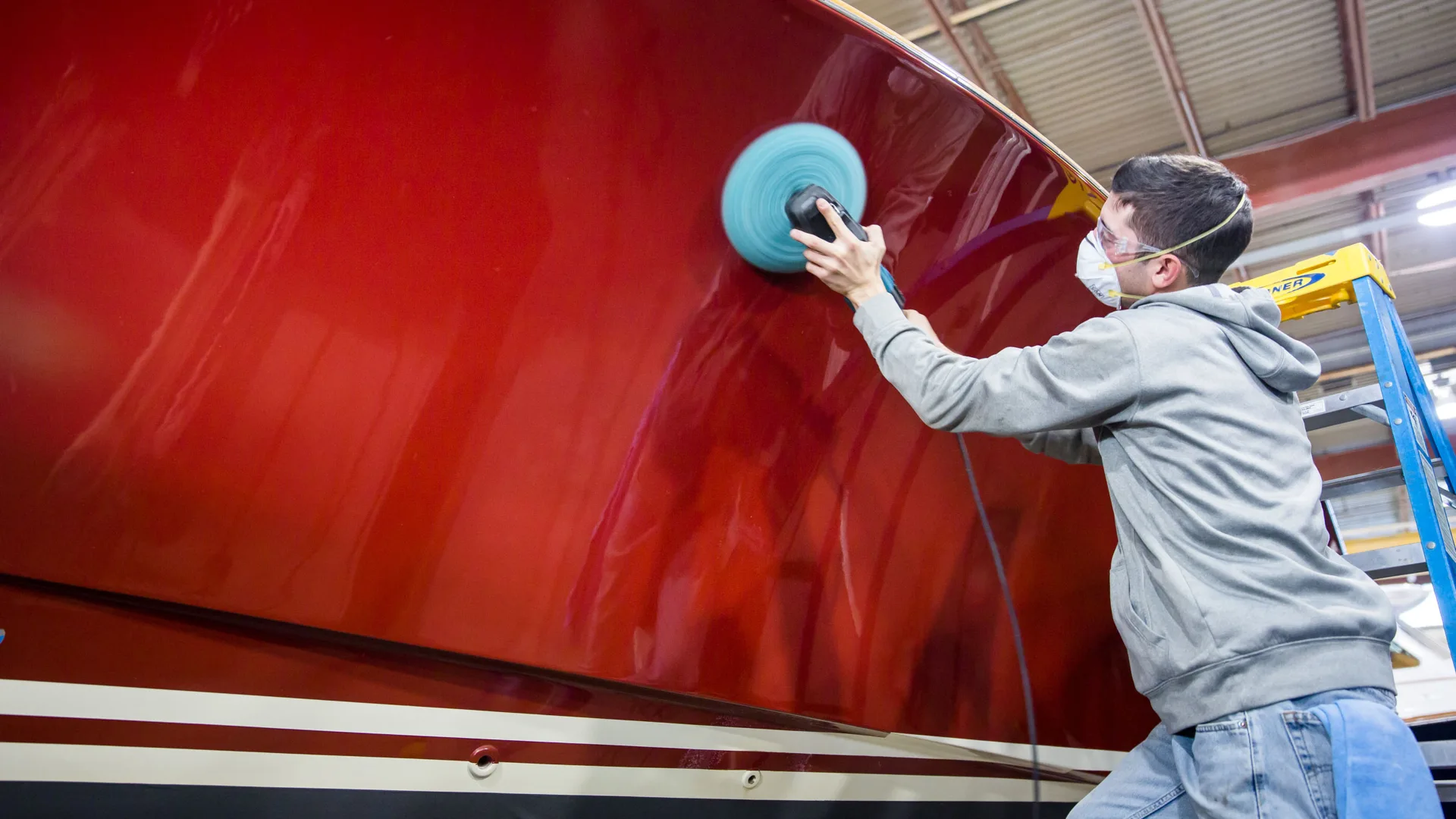 Technician polishing the red hull of a boat in Stamford